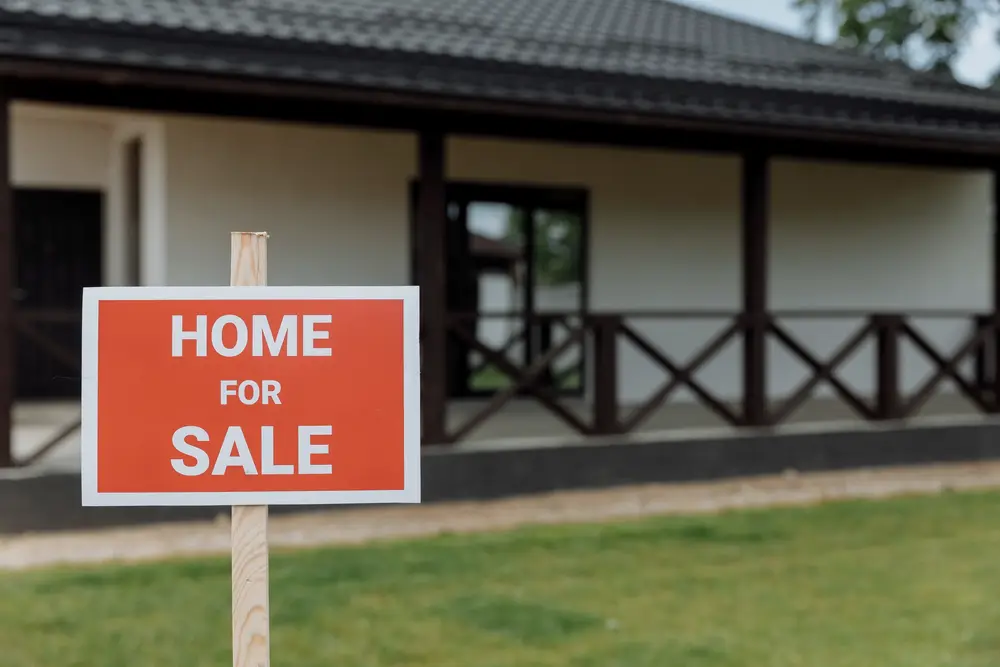 Red home for sale sign on a lawn in front of a porch