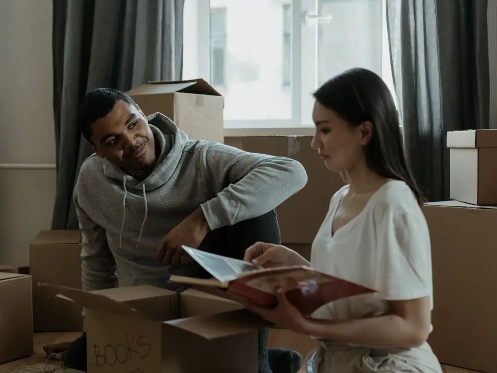 Couple sitting among moving boxes in their new home, looking at a photo album